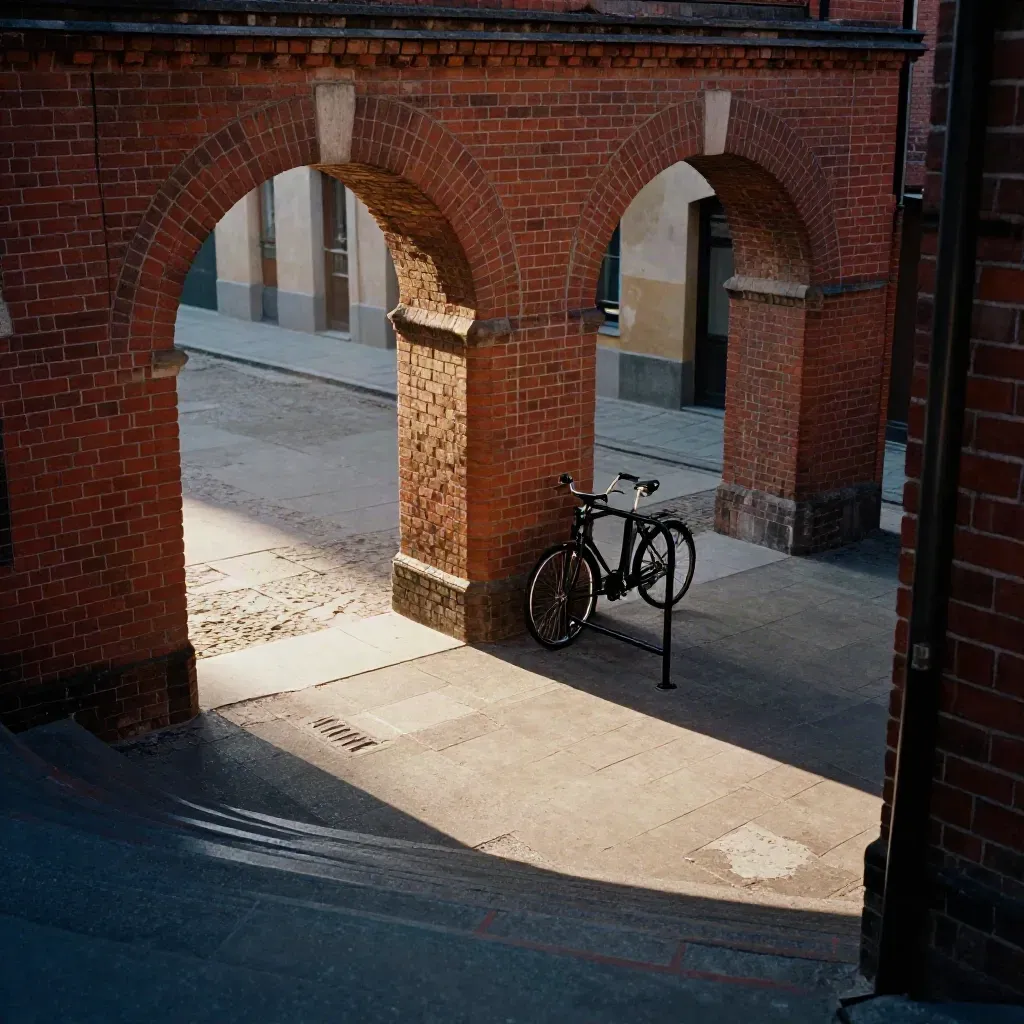 Leerer Berliner Innenhof mit Backsteinbögen, Fahrradständer und Sonnenstrahl am Treppenpodest.